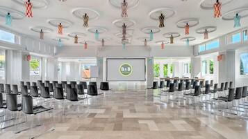 Un salón de conferencias con una pantalla grande que muestra el logotipo de B&B HOTELS, sillas dispuestas y un diseño de techo moderno.