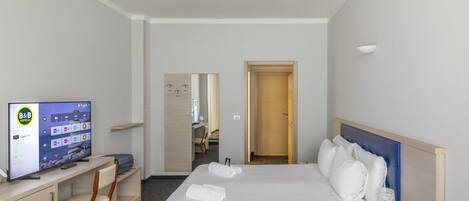 Een hotelkamer met een bed, een bureau met een televisie, een stoel en een deur naar een badkamer.