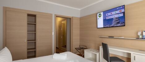 A hotel room with a bed, a desk, a chair, a TV mounted on the wall, and a wardrobe.