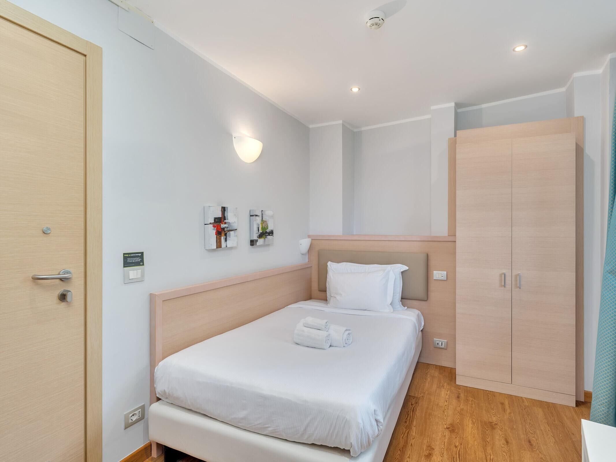 A hotel room with a bed, a wardrobe, and a wall-mounted light fixture.