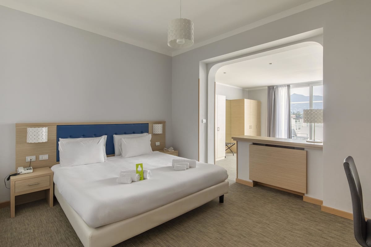 A hotel room with a large bed, bedside tables, a desk, and a view of the city.