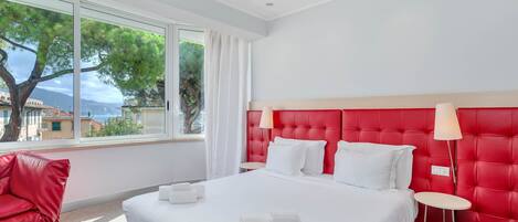 Habitación de hotel con una cama grande, cabecera roja y vistas a árboles y edificios desde la ventana.