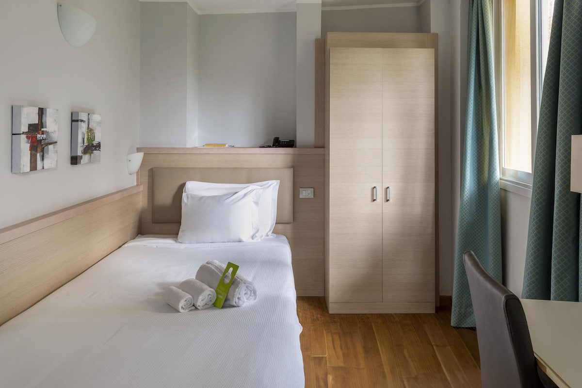 A hotel room with a bed, a wardrobe, a desk, and a window with curtains.