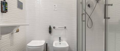 Un baño moderno con inodoro, bidé y cabina de ducha con mampara de vidrio.