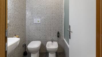 A bathroom with a white sink, toilet, and bidet, tiled walls, and a door with a handle.