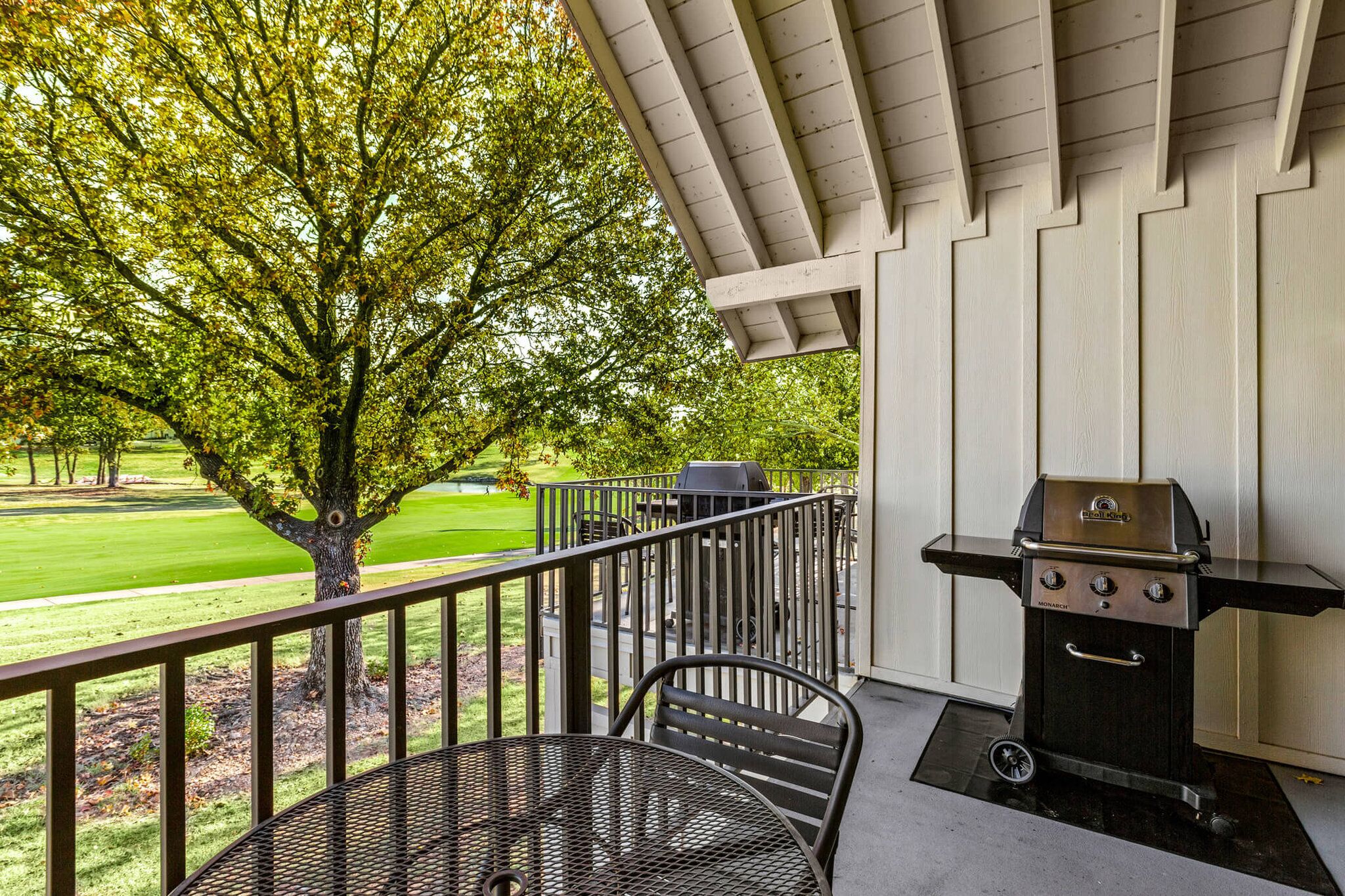 Un balcon avec un barbecue, une table et une vue sur un parc.