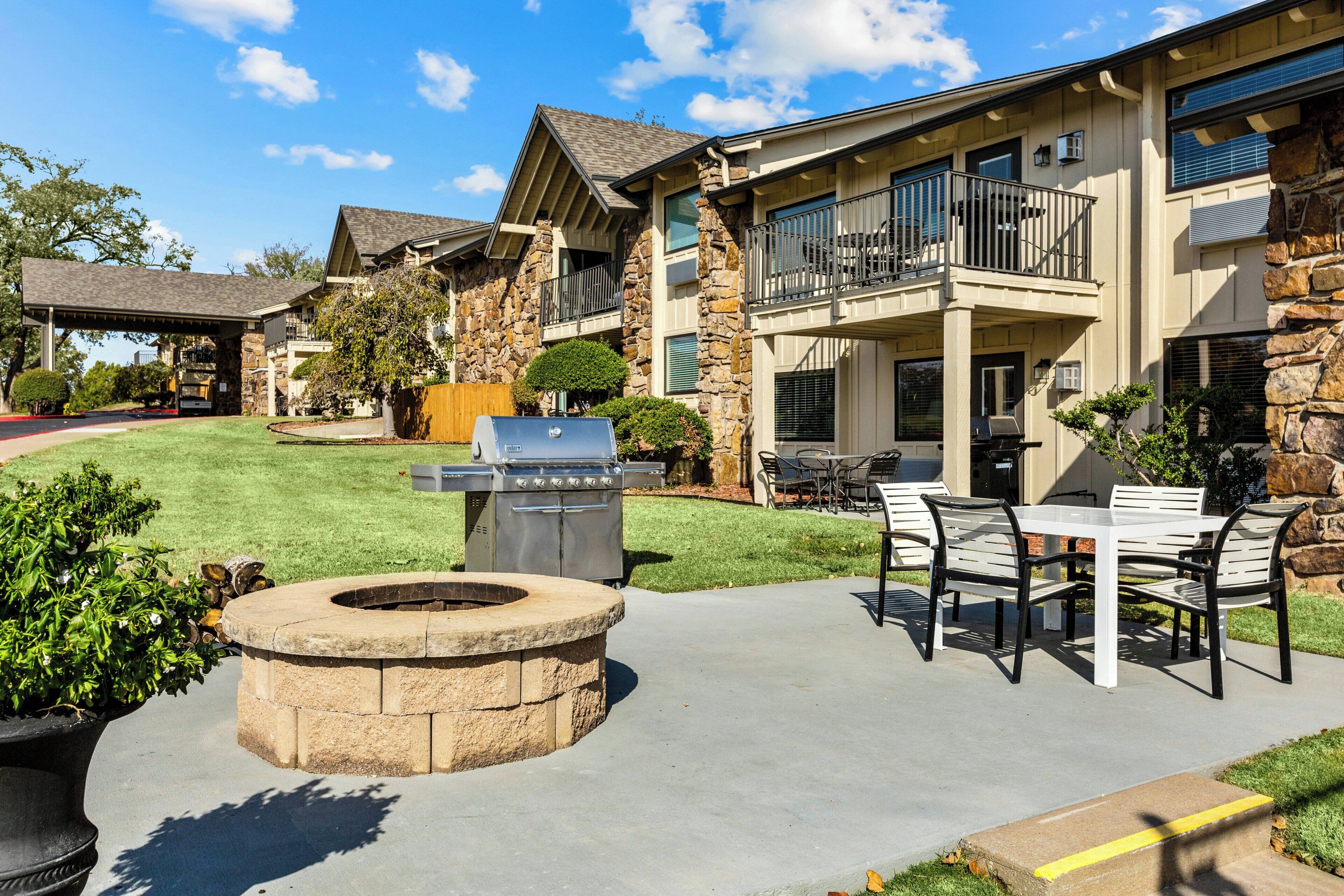 Un espace patio avec un foyer en pierre, des sièges d’extérieur et un barbecue.