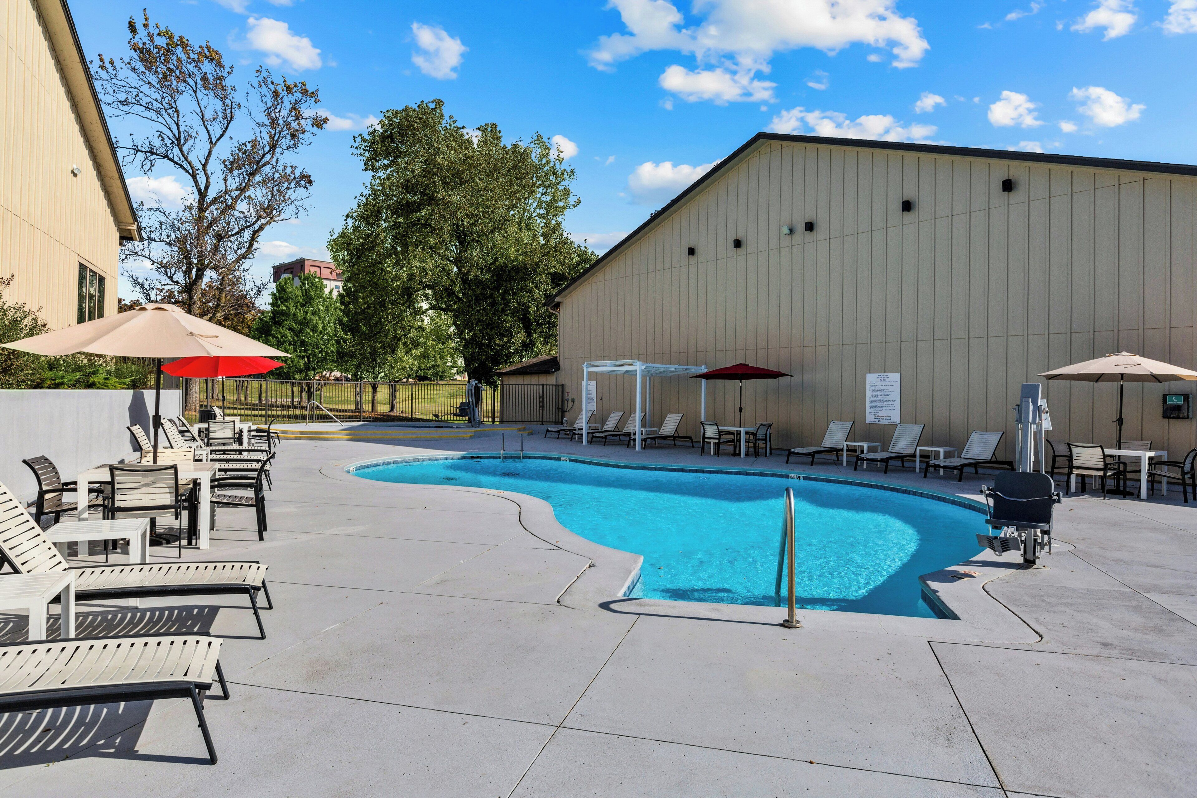 A swimming pool area with lounge chairs and umbrellas, surrounded by a building.
