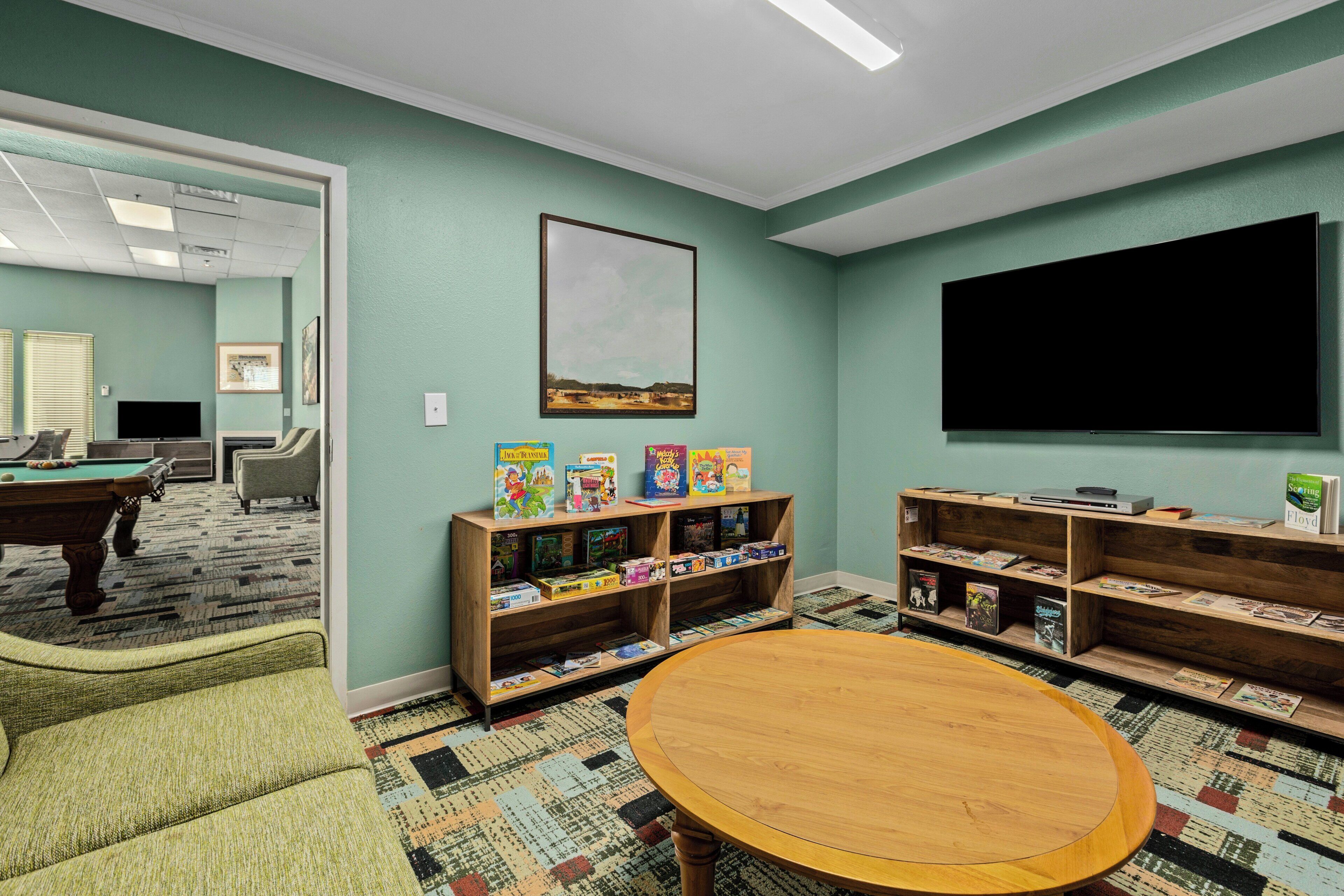 A room with a pool table, comfortable seating, a bookshelf with various books, and a television.