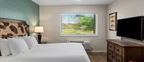Habitación de hotel con una cama grande, televisión, ventana con vistas a vegetación y cómoda de madera.