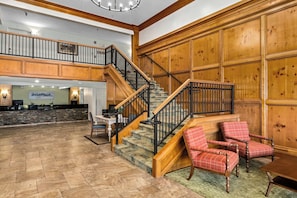 A spacious lobby with a wooden staircase, a reception desk, and a seating area with plaid chairs. - WorldMark Grand Lake (Afton)