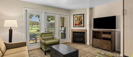 A living room with a sofa, armchair, coffee table, fireplace, television, and a view of the outdoors.