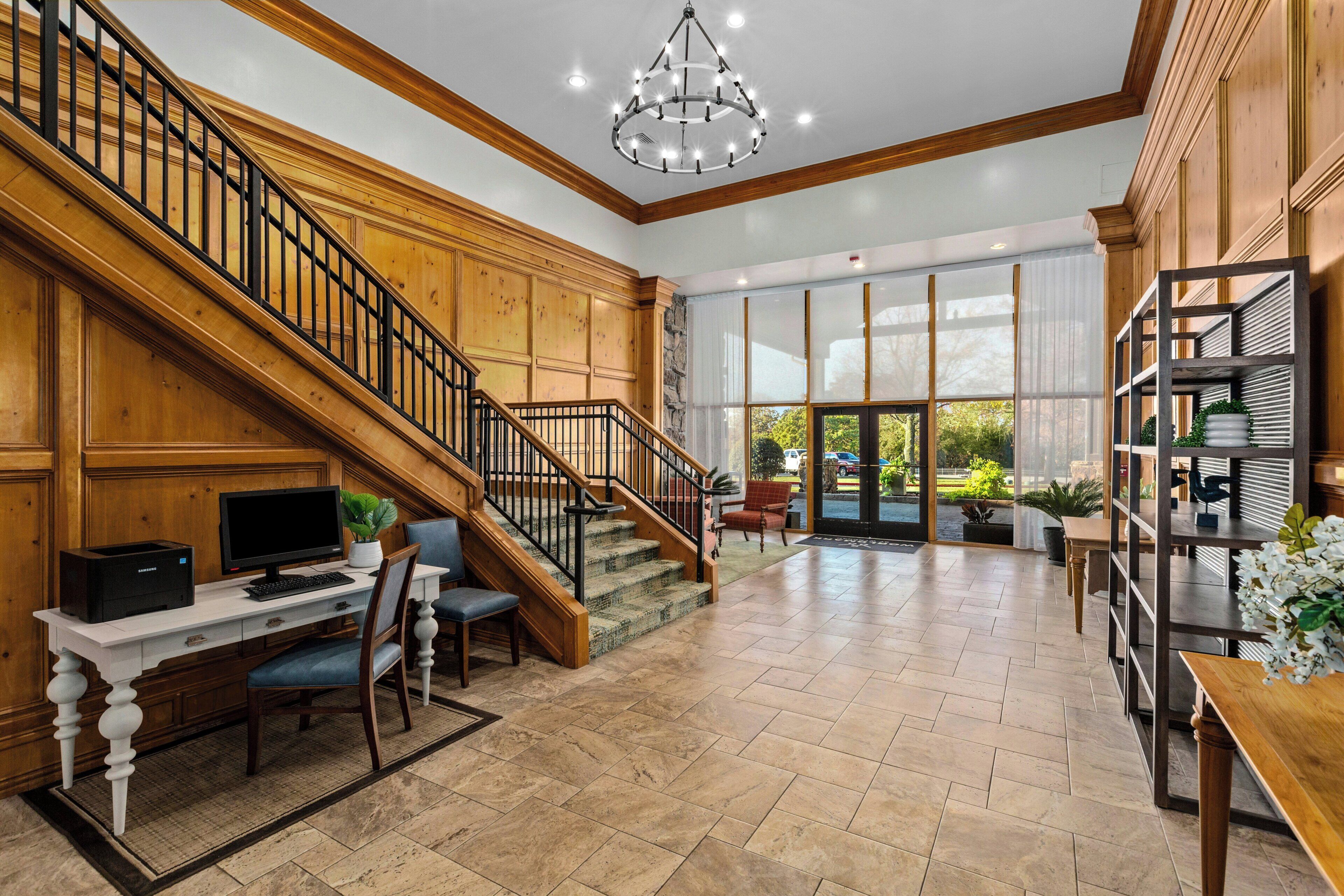 A spacious interior with a grand staircase, a computer desk, and a large window offering a view of the outdoors.