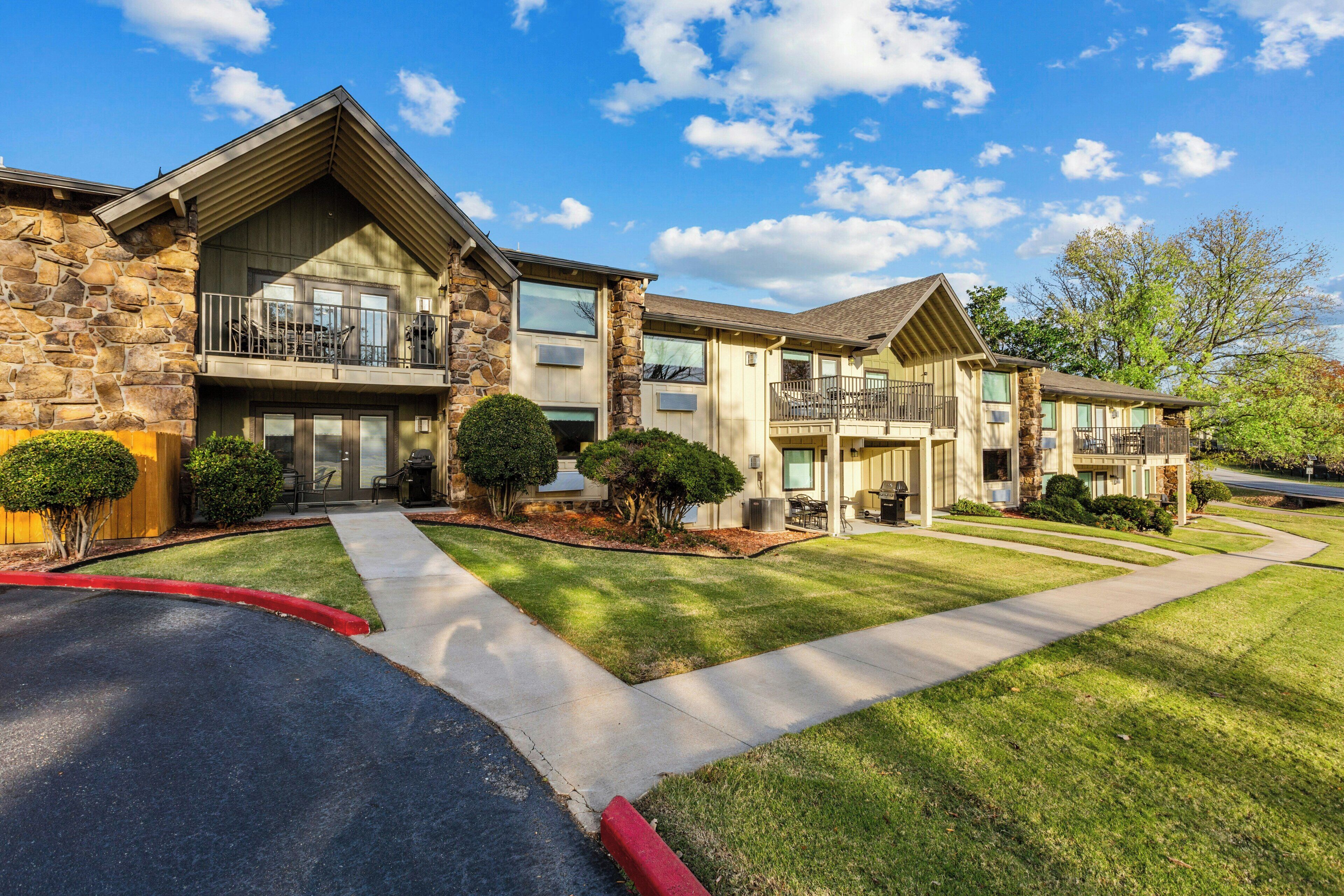 A multi-story residential building with a stone facade, multiple balconies, and a well-maintained lawn.