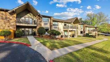 A multi-story residential building with a stone facade, multiple balconies, and a well-maintained lawn.