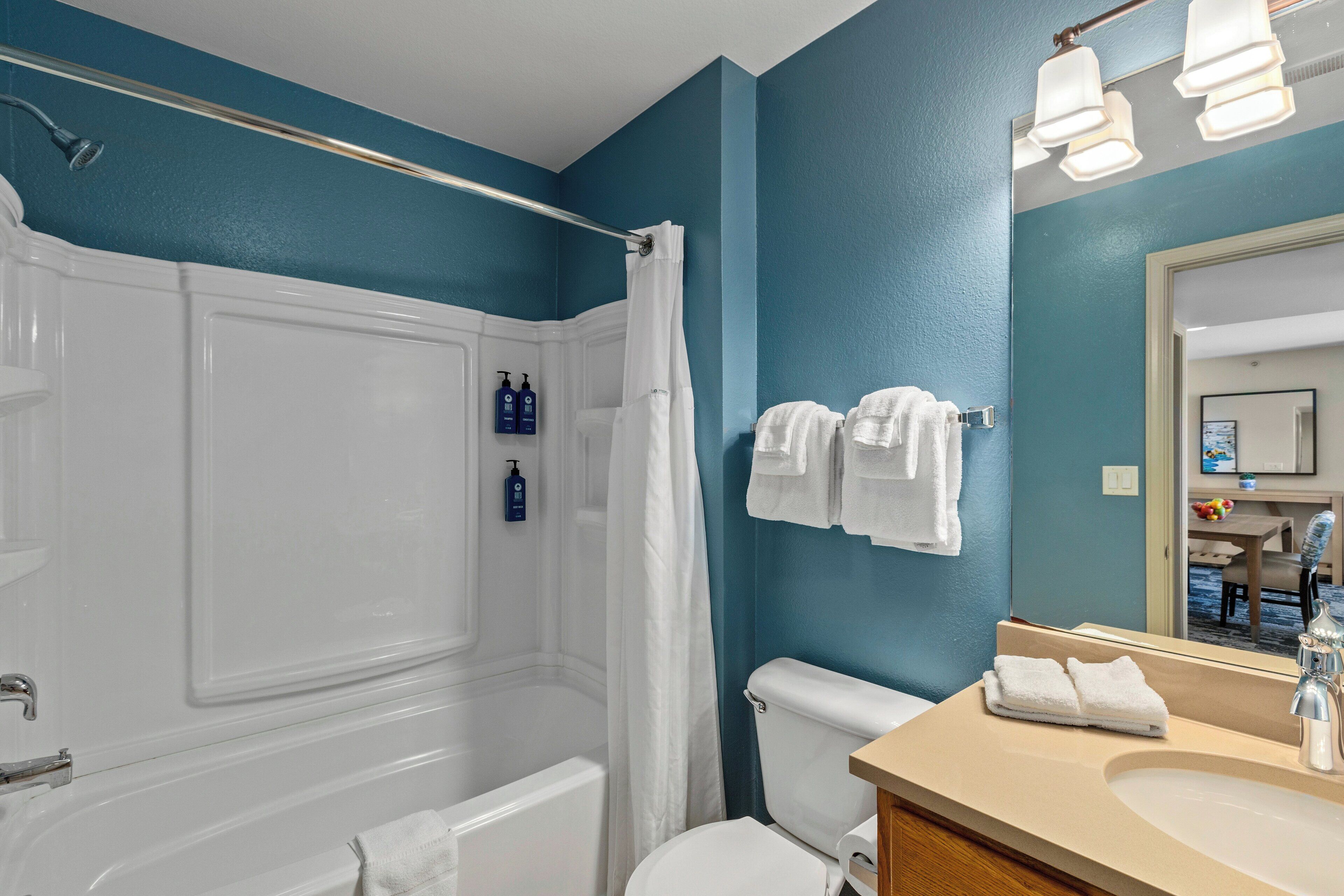 A bathroom with a bathtub, toilet, and sink. There are towels hanging on the wall and a shower curtain.