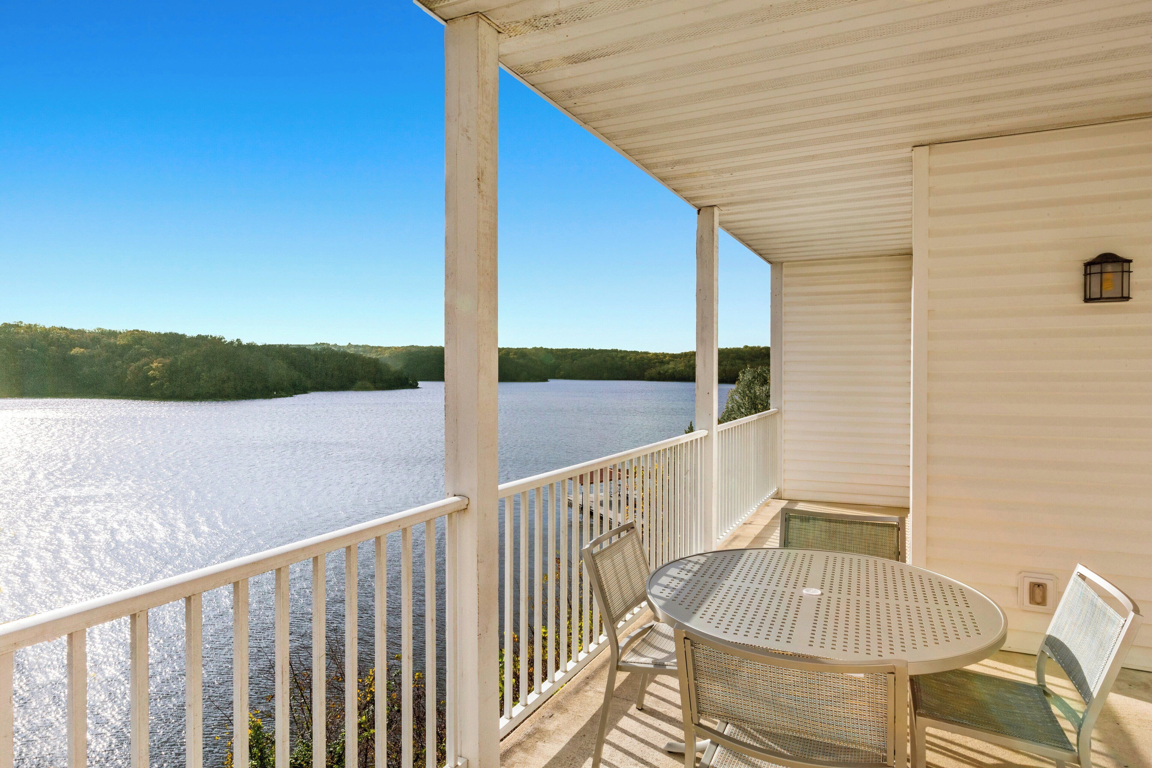 A balcony with a view of a lake, a round table, and two chairs.
