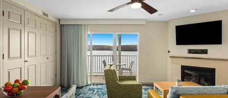 Une chambre d’hôtel avec un balcon, une table à manger avec des chaises, un canapé, un téléviseur fixé au mur et un ventilateur de plafond.