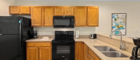 A modern kitchen with wooden cabinets, a black refrigerator, a microwave, an oven, a sink, and a dishwasher.