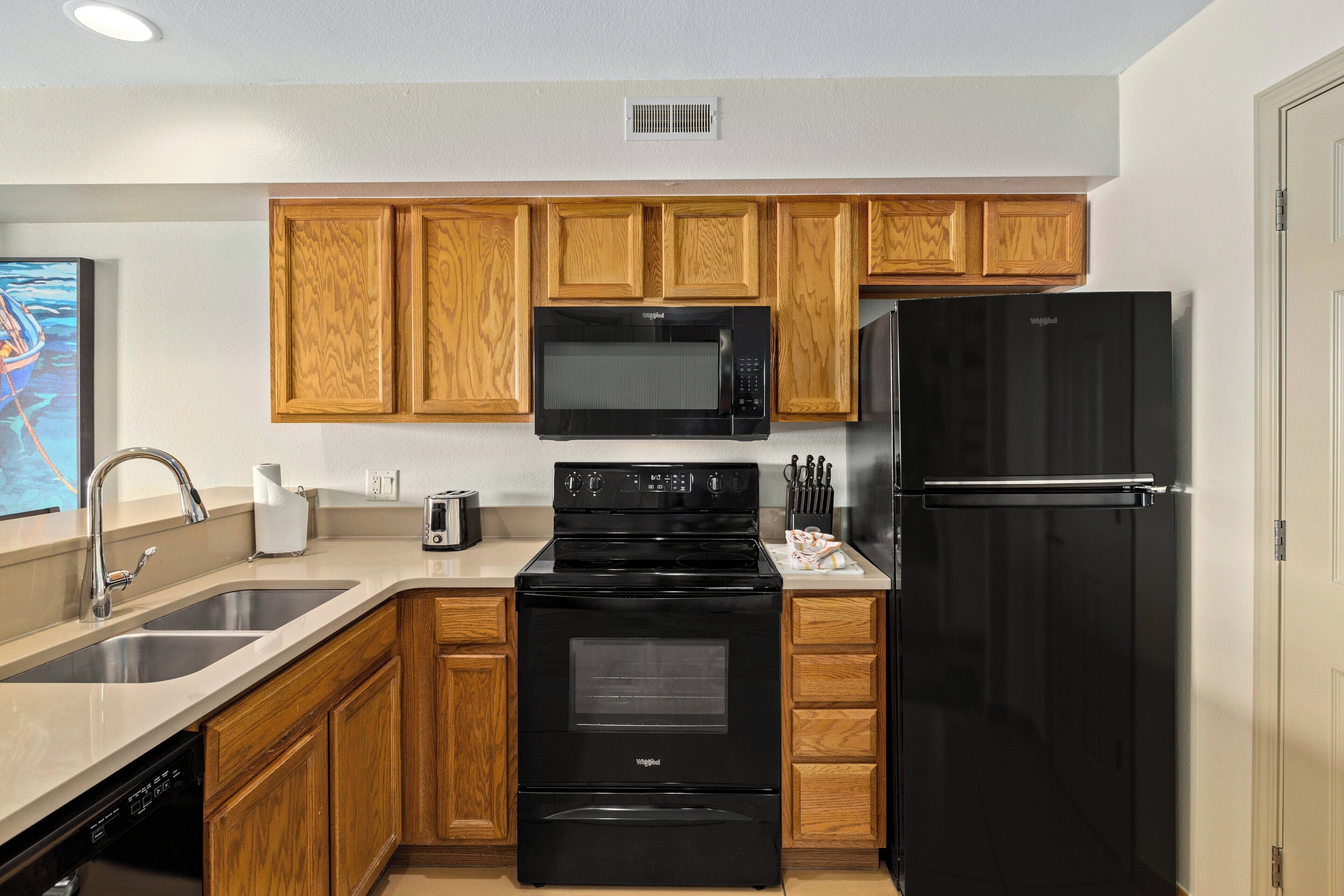 A kitchen with wooden cabinets, a black microwave, a black refrigerator, a stove, and a dishwasher.