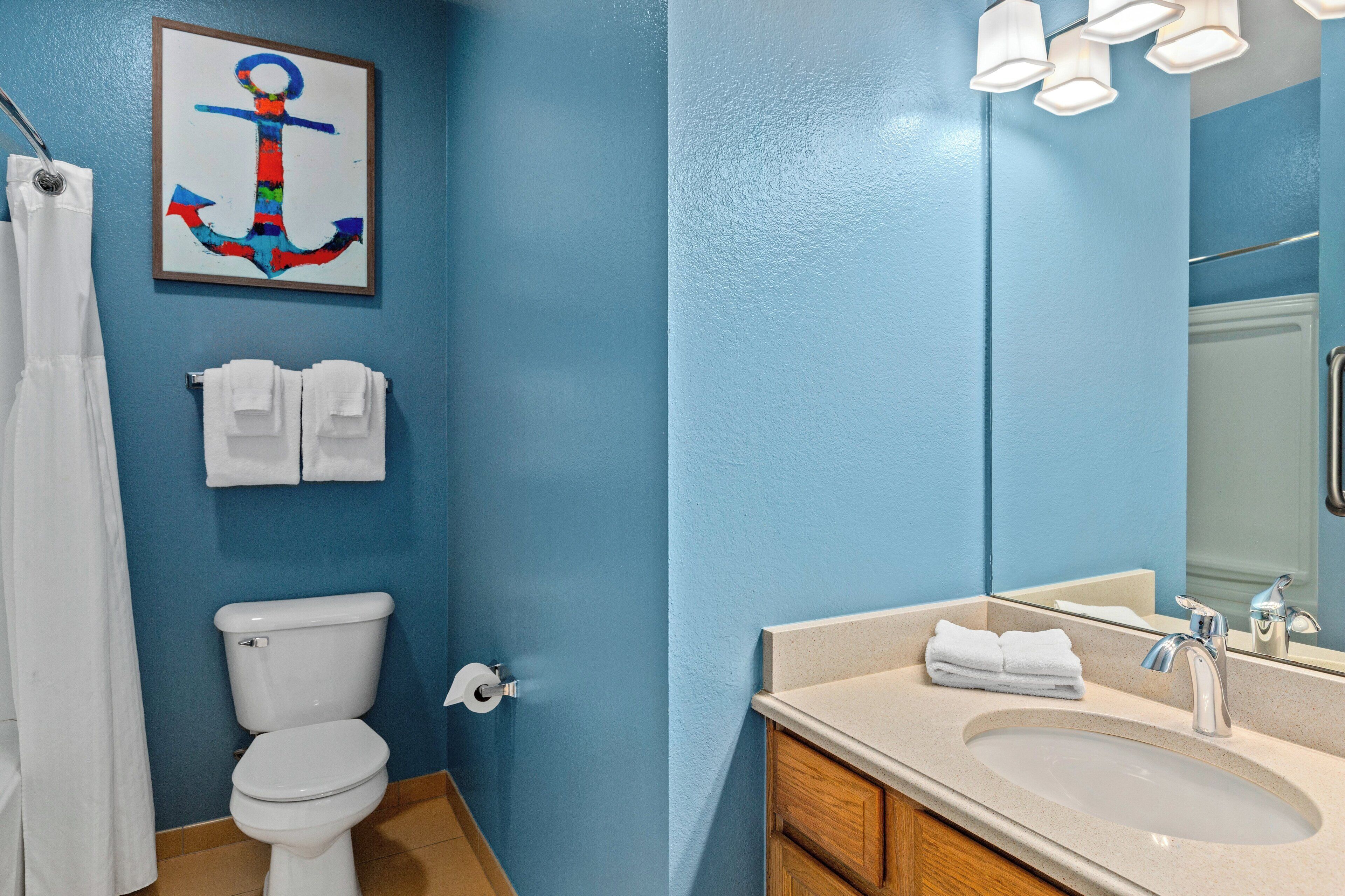 Une salle de bain avec un mur bleu, des toilettes blanches, un lavabo avec un miroir et un tableau représentant une ancre.