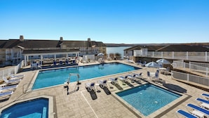 A swimming pool with lounge chairs and umbrellas, surrounded by buildings with a view of the water. - WorldMark Lake of the Ozarks (Osage Beach)