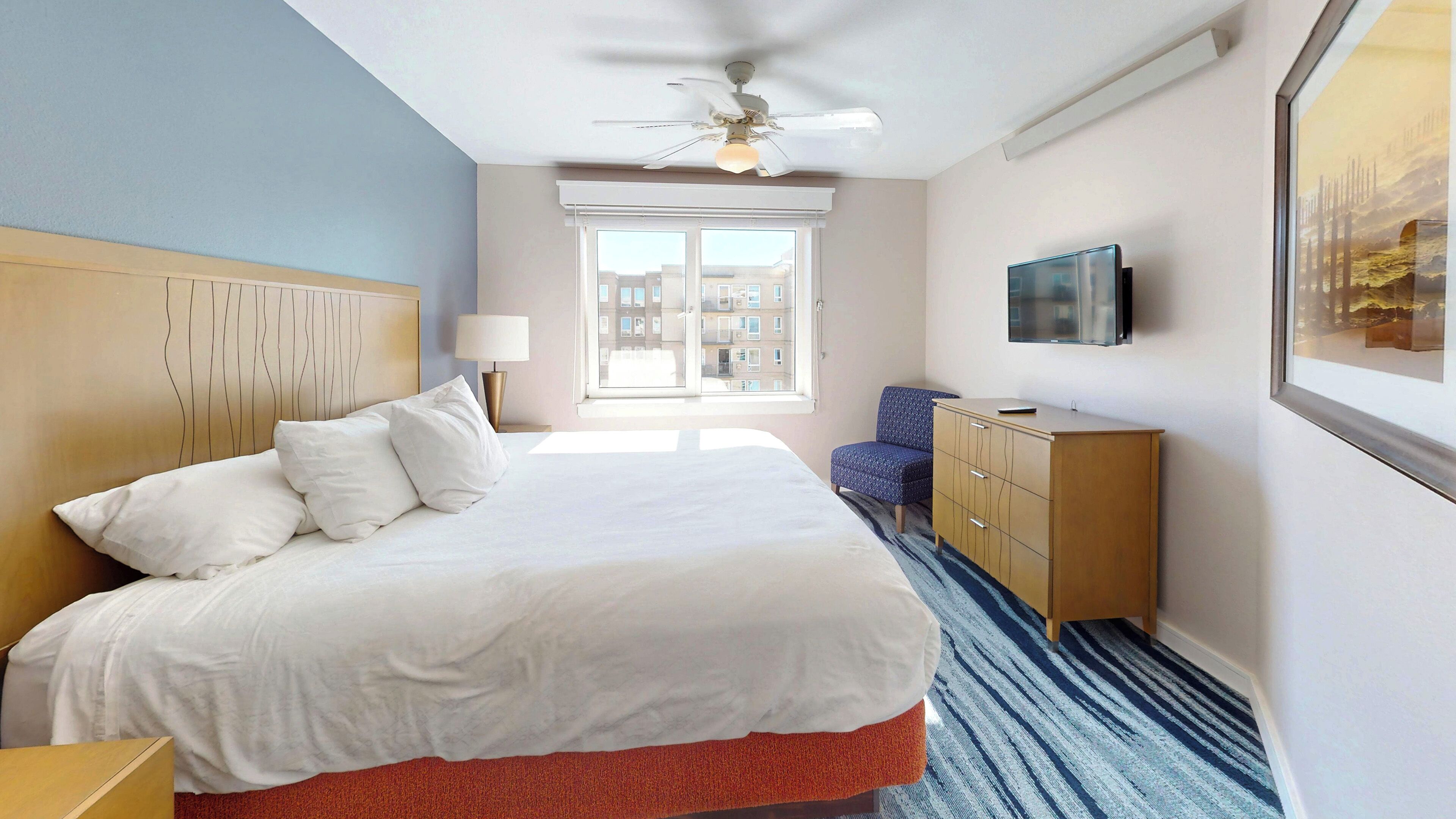 A hotel room with a bed, a desk, a chair, a TV, and a window with a view of buildings.