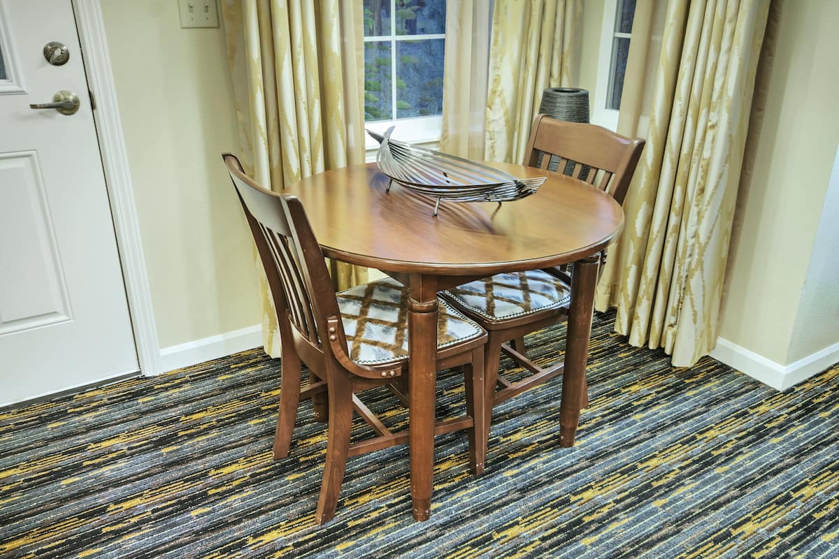 A dining area with a round wooden table, two chairs, and a magazine rack.