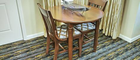 A dining area with a round wooden table, two chairs, and a magazine rack.