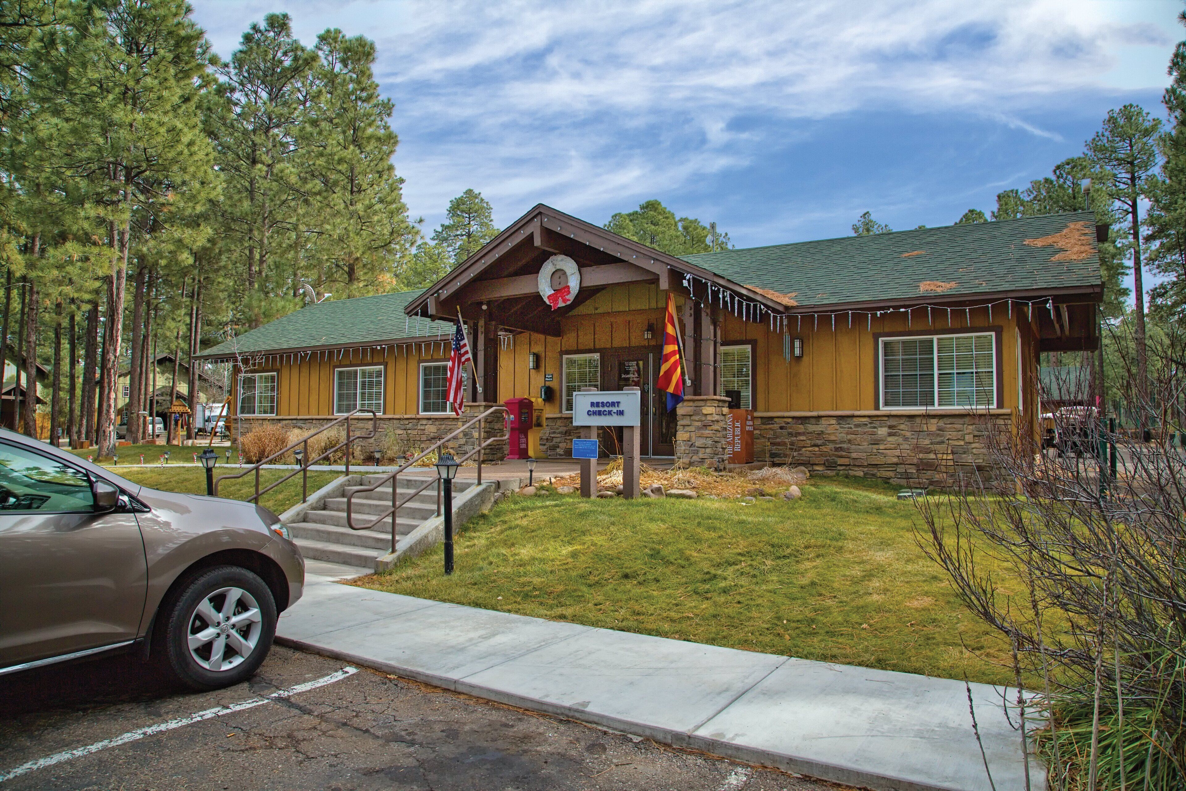 A lodge with a stone facade, a green roof, and a check-in sign.
