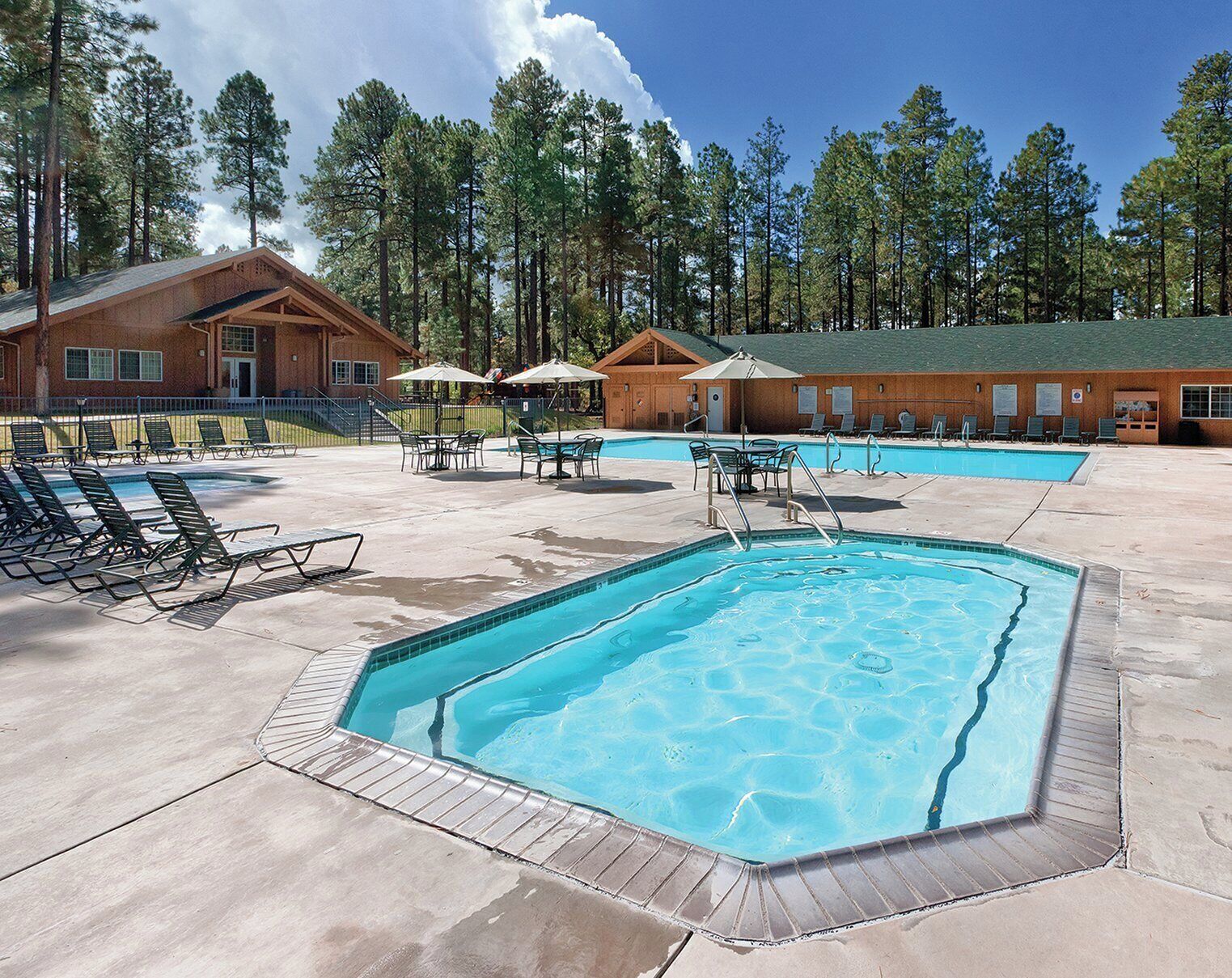 A pool area with lounge chairs and umbrellas, surrounded by wooden cabins.