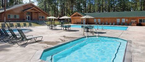 A pool area with lounge chairs and umbrellas, surrounded by wooden cabins.