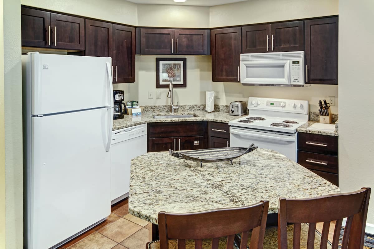A kitchen with dark wooden cabinets, a white refrigerator, a microwave, a stove, and a granite countertop.