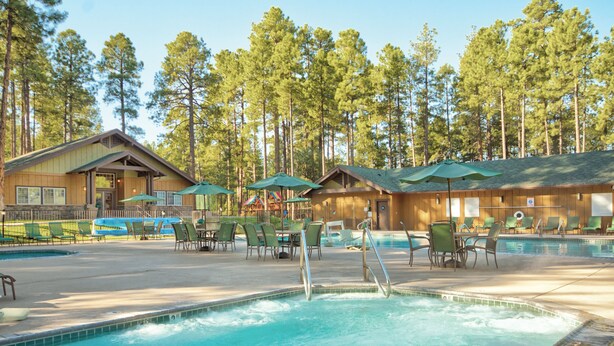 A pool area with lounge chairs and umbrellas, surrounded by cabins and tall trees. - WorldMark Pinetop (Pinetop)