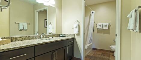 A modern bathroom with a granite countertop, dark cabinets, a large mirror, and a shower curtain.