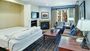 A hotel room with a bed, a sofa, a coffee table, a fireplace, a television, and a window with curtains. - WorldMark Pinetop (Pinetop)