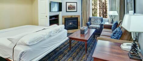 A hotel room with a bed, a sofa, a coffee table, a fireplace, a television, and a window with curtains.
