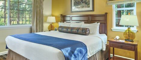 A hotel room with a large bed, a nightstand with a lamp, a window with curtains, and a ceiling fan.