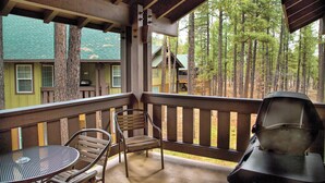 A covered outdoor area with a metal table and chairs, a grill, and a view of a forested area with buildings in the background. - WorldMark Pinetop (Pinetop)