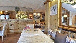A cozy, rustic interior with wooden walls and furniture, a bar area with bottles, and a dining space with a long table and chairs. - Hotel Da Compagnoni (Valtournenche)