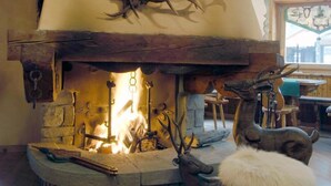 A rustic fireplace with antlers, a wooden bench, and a fur-covered ottoman. - Hotel Da Compagnoni (Valtournenche)