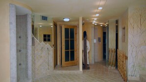 A hallway with a tiled floor, a wooden door, and a person in white attire. - Hotel Da Compagnoni (Valtournenche)
