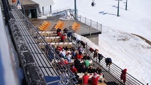 A ski lift area with people seated on benches and tables, a ski lift in operation, and a building in the background. - Hotel Lo Stambecco (Valtournenche)