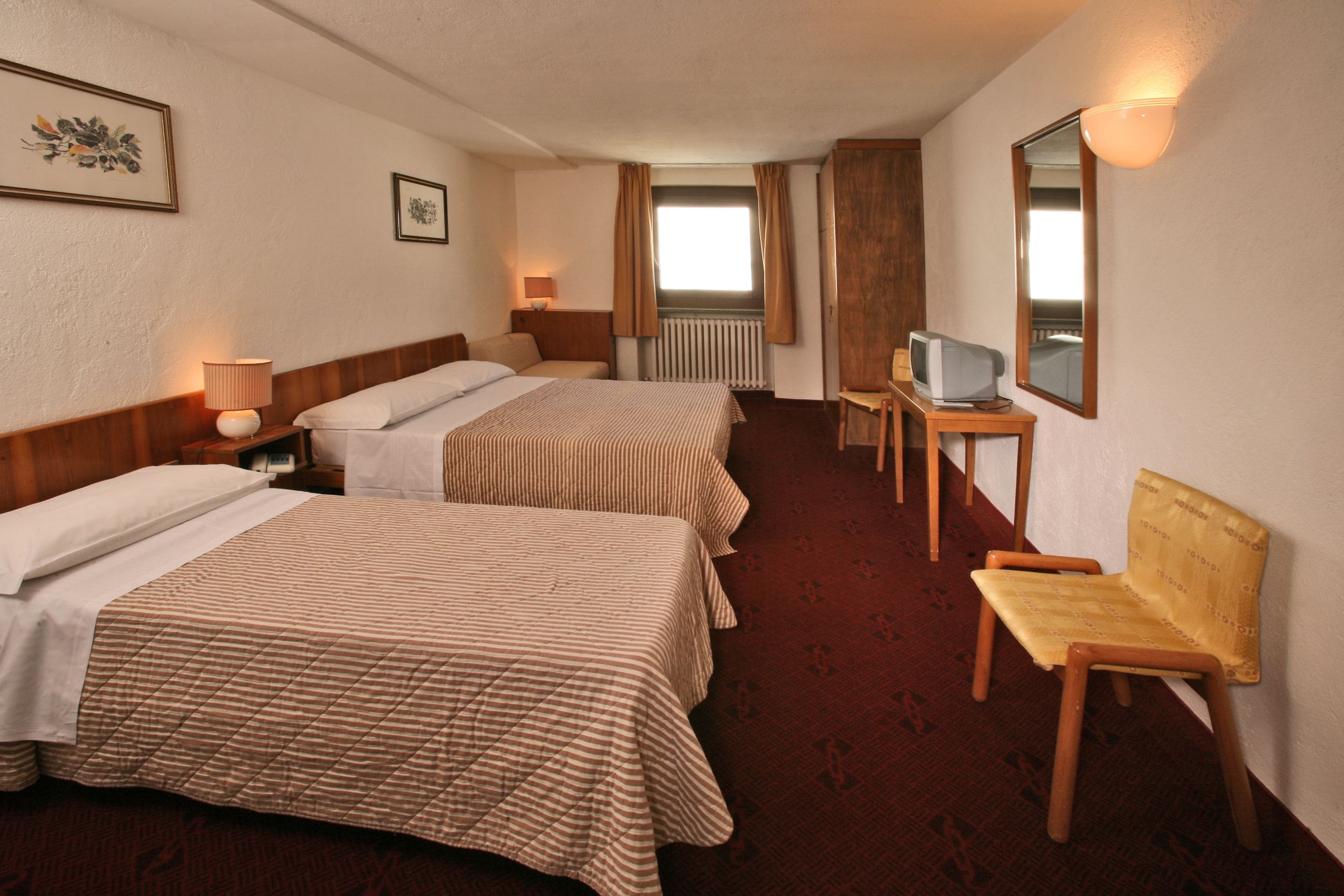 Ein Hotelzimmer mit zwei Betten, einem Sessel, einem Fernseher und einer Heizung.
