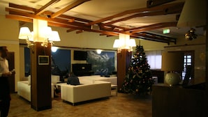A lobby with a stone floor, white sofas, wooden beams, and a Christmas tree. - Hotel Lo Stambecco (Valtournenche)