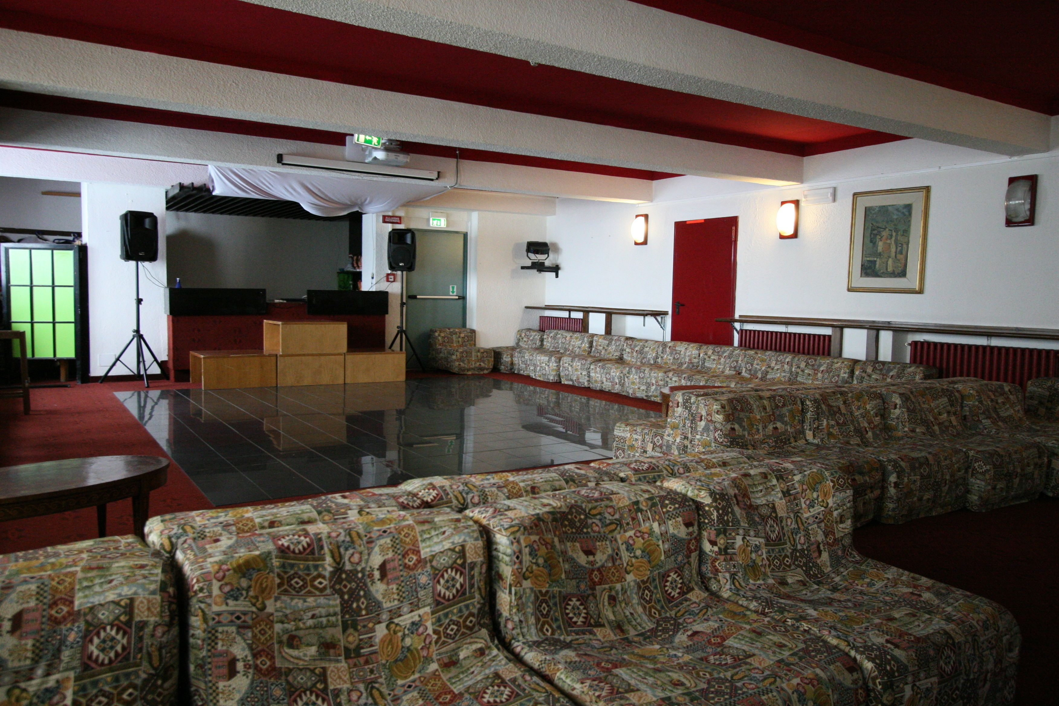 A spacious lounge area with patterned sofas, a projector screen, and a speaker setup.
