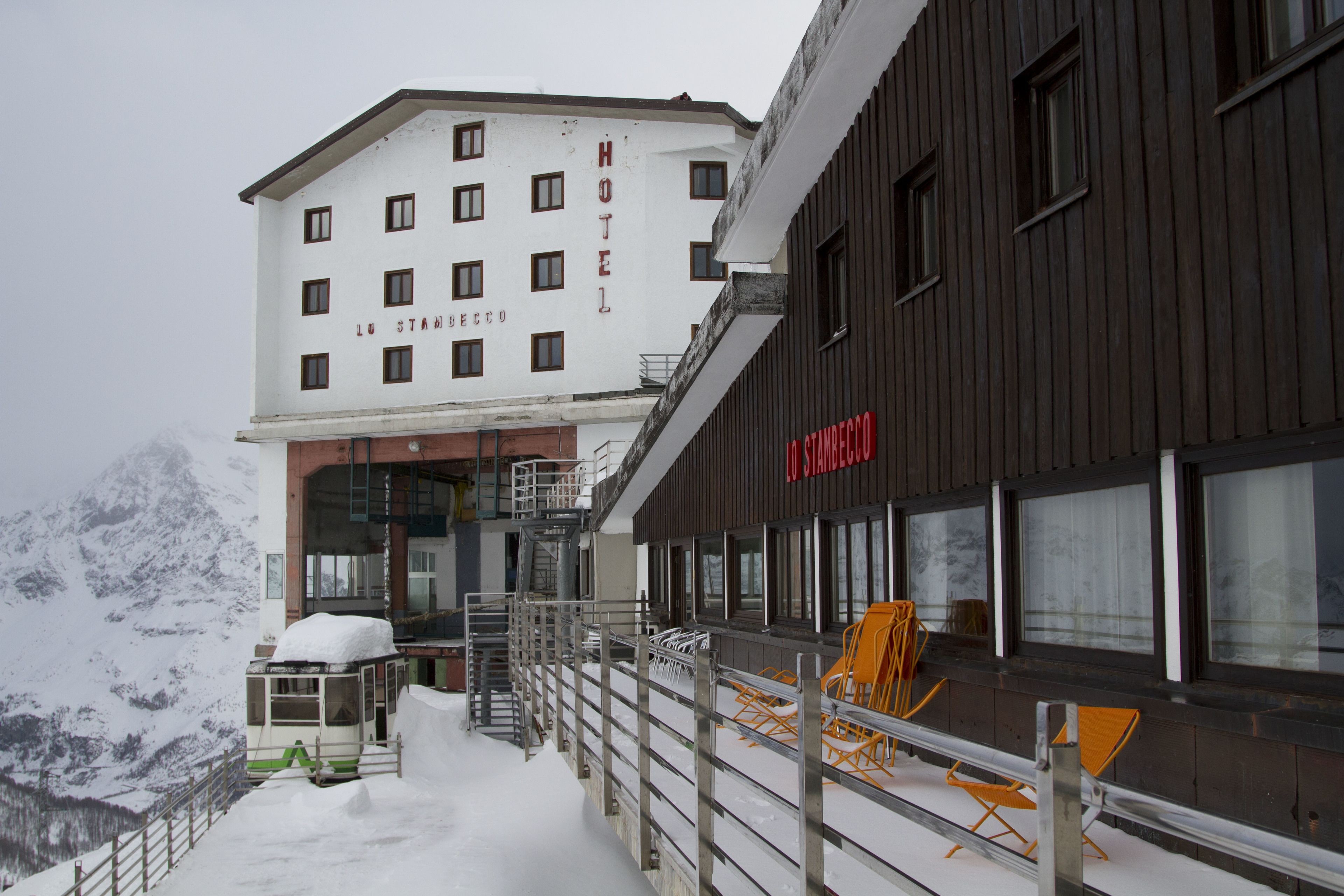 A hotel with a snow-covered exterior, a visible staircase, and a mountain backdrop.