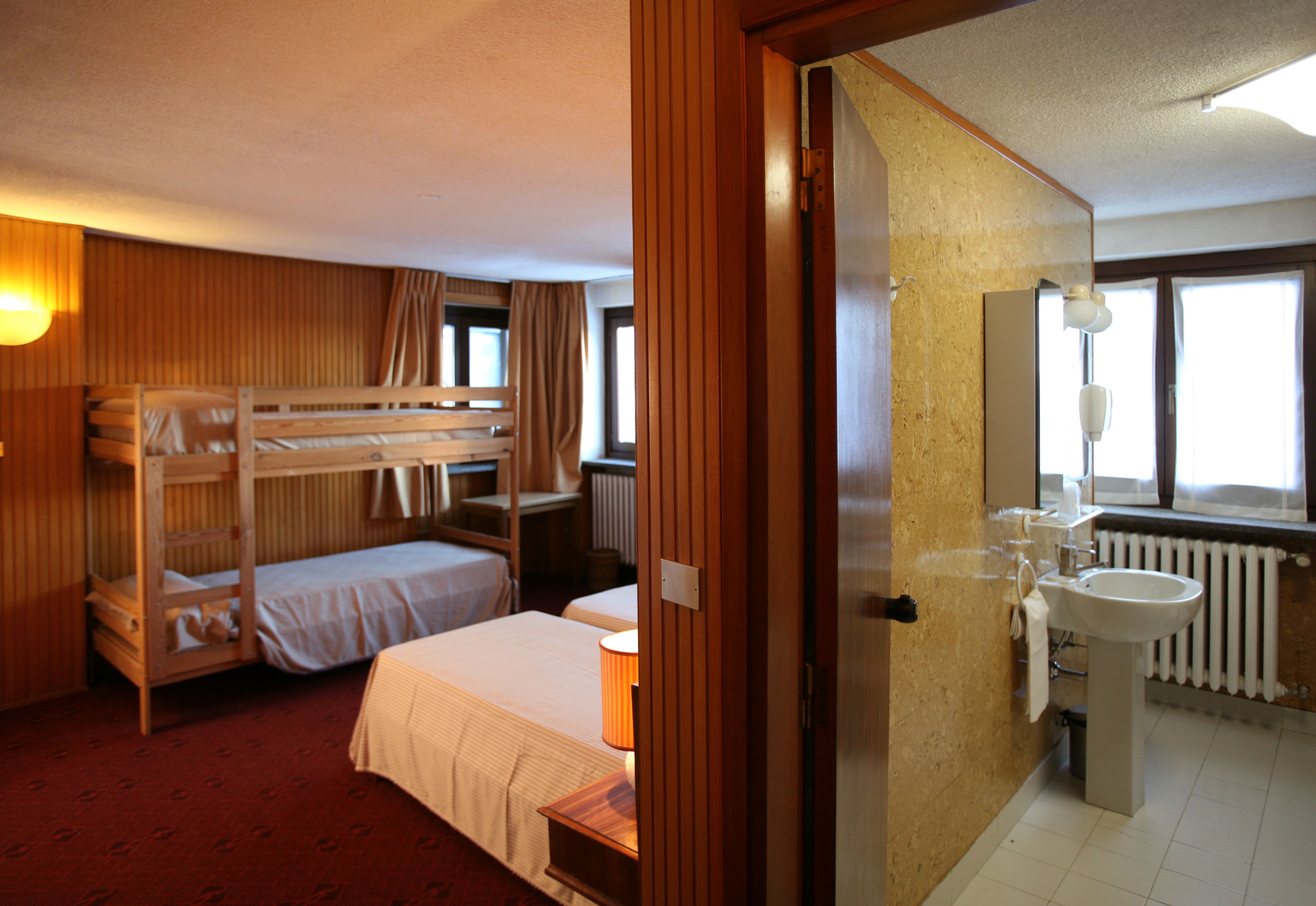 Habitación de hotel con literas, baño con lavamanos y espejo, y ventana que deja entrar luz natural.