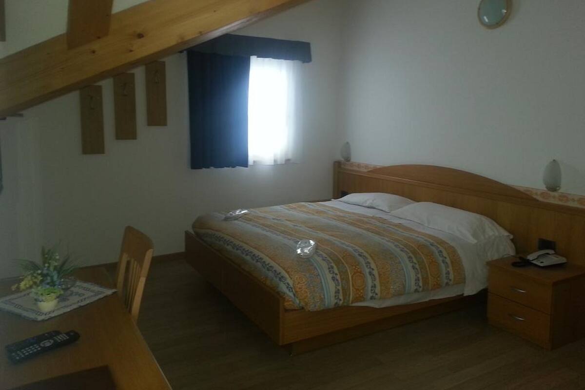 Un dormitorio con cama de madera, una mesita de noche, un escritorio con silla y una ventana con cortinas.