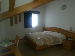 Un dormitorio con cama de madera, una mesita de noche, un escritorio con silla y una ventana con cortinas.